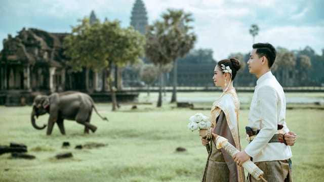 Elegant Cambodian couple in traditional attire at Angkor Wat with an elephant in the background.