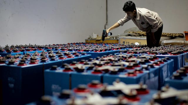 A worker checking many industrial batteries inside a facility. Indoor, industrial setting.