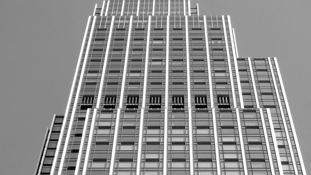 From below of black and white modern multistory commercial building with geometric facade and glass windows against cloudless sky in city