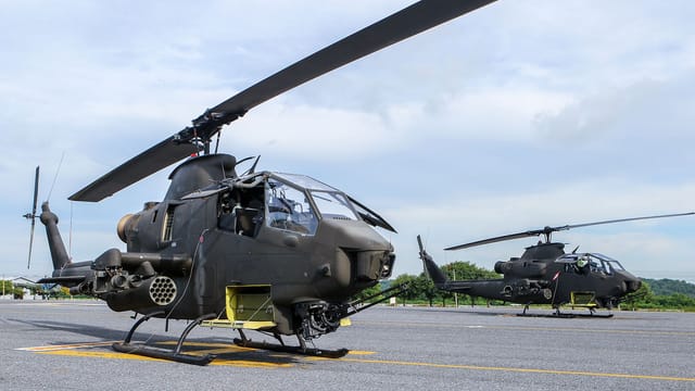 Two military helicopters parked on an outdoor runway on a clear day.