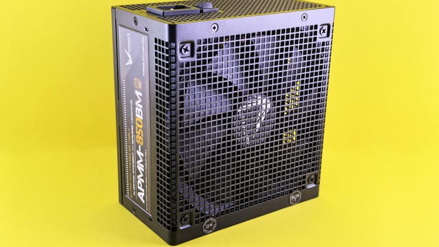 Black computer power supply unit with fan displayed against yellow background.