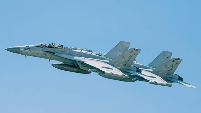 F/A-18 Super Hornets flying in formation in a clear blue sky over New York.