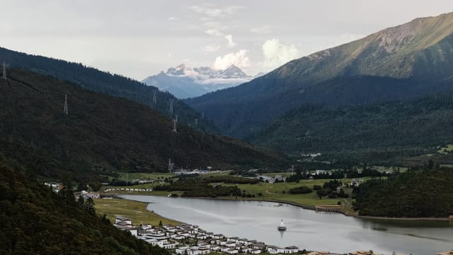 Beautiful valley in Tibet with a river, traditional houses, and snow-capped mountains in the distance.