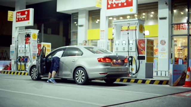 A person refuels their car at an illuminated Shell gas station at night.
