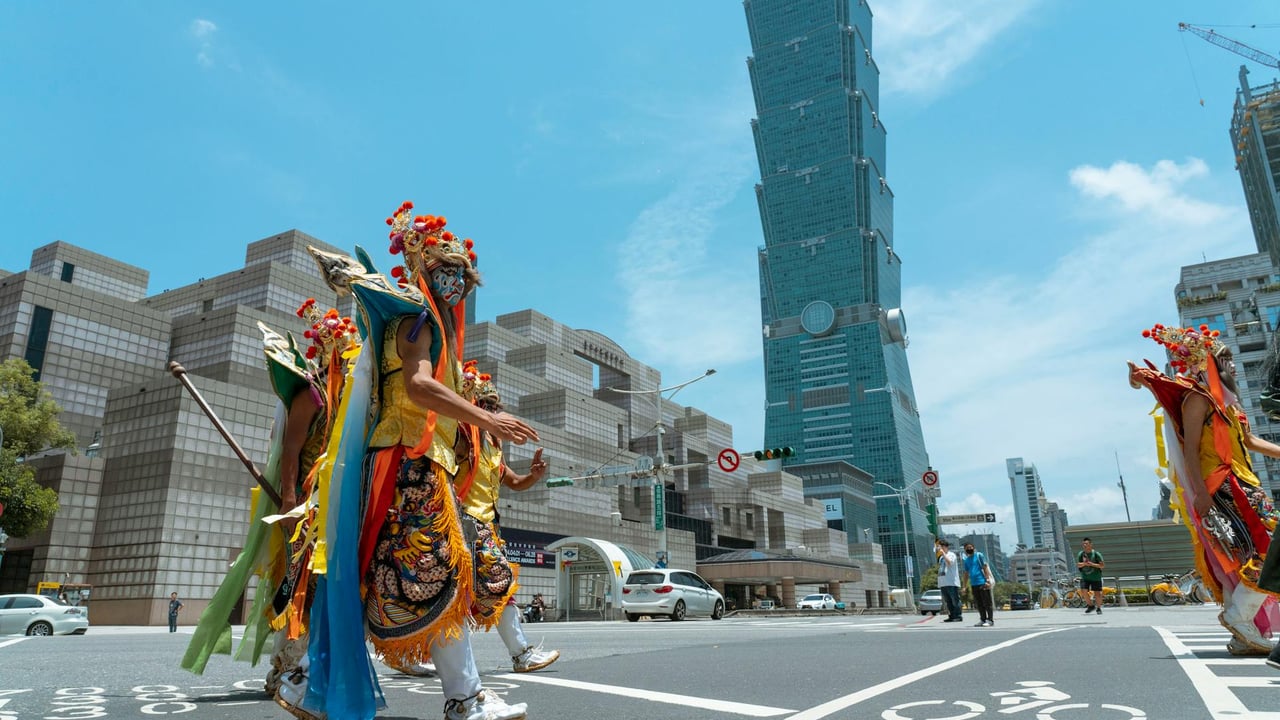 Colorful performers in traditional costumes cross the street near Taipei 101 on a sunny day.
