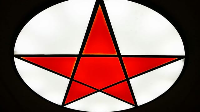 Close-up of an illuminated stained glass featuring a red star with geometric patterns.