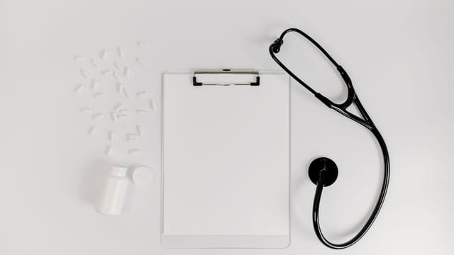 Flat lay of clipboard, pills, and stethoscope for medical use.