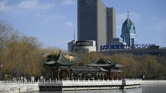 A scenic view of a traditional Chinese pavilion by a lake with modern skyscrapers in the background.