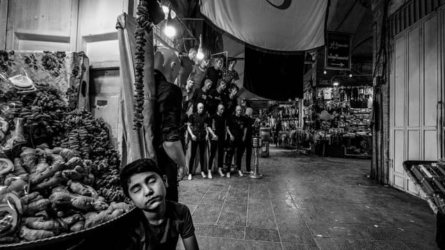 A serene black and white portrayal of a boy in the bustling İsfahan bazaar at night.