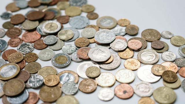 A diverse collection of international coins spread across a white surface, showcasing various currencies and designs.