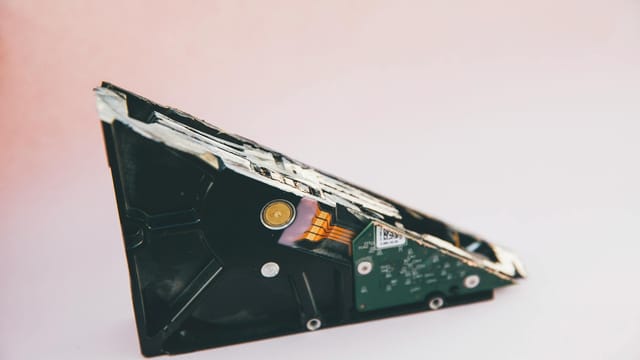 Close-up of a broken hard disk drive showing internal components on a pink background.