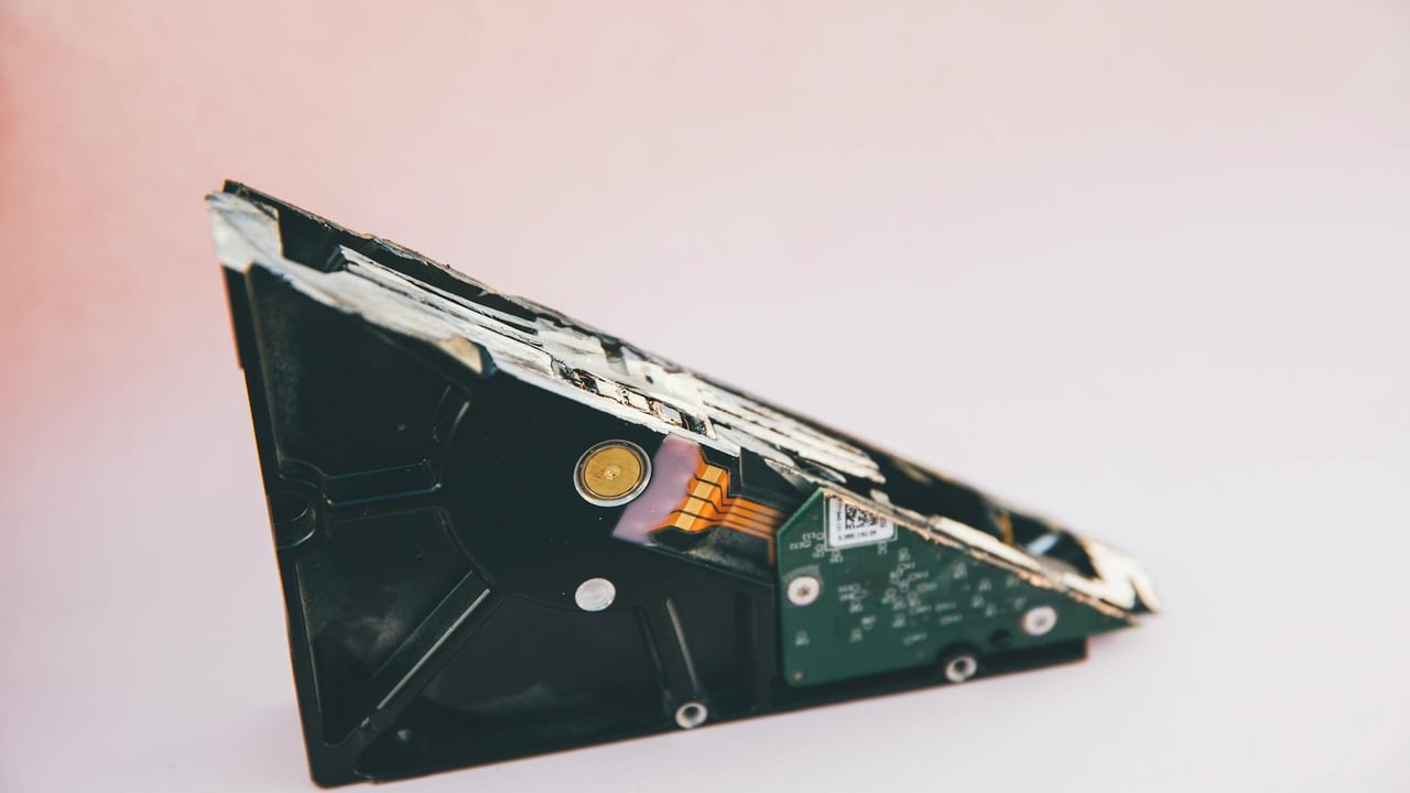 Close-up of a broken hard disk drive showing internal components on a pink background.