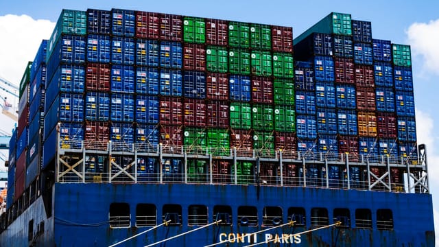 Illustrative image: Stacked cargo containers on a massive ship at the harbor, symbolizing global trade.