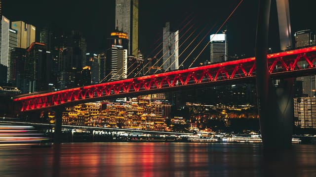 Stunning night view of Chongqing with illuminated bridge and city lights reflecting on water.