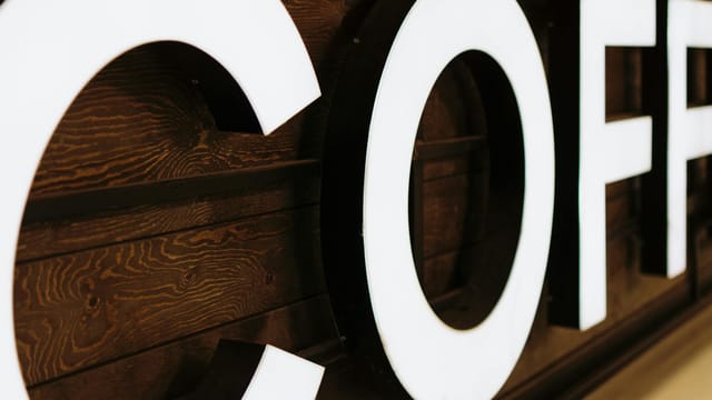 A close-up view of a large, illuminated coffee sign with wooden background indoors.