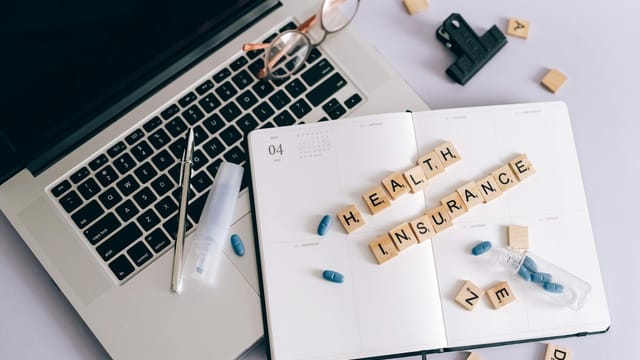 Flat lay of a laptop, notebook, and pills depicting health insurance planning.