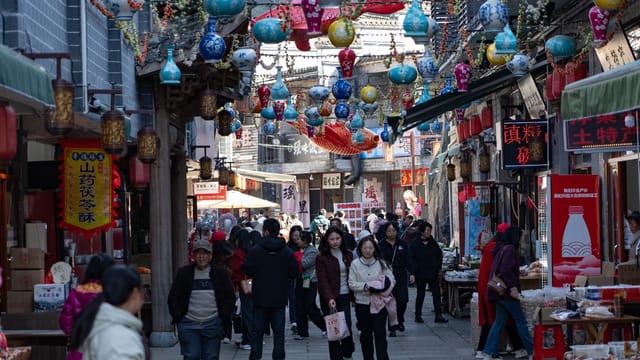 Bustling pedestrian street market with colorful hanging lanterns and diverse crowd of shoppers.