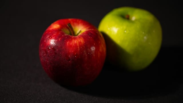 Close-up of a red and green apple with water droplets, showcasing freshness and vibrant colors.