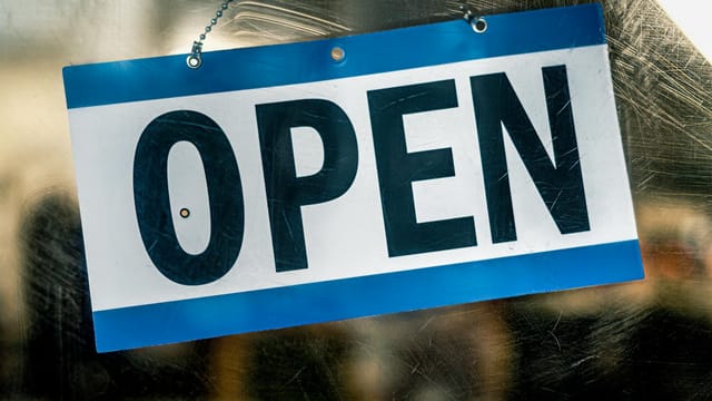 A blue and white open sign hanging on a retail shop's glass door.