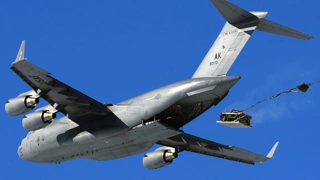 United States Air Force aircraft performing an airdrop maneuver in clear sky.