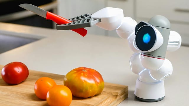 Innovative robot using a knife on a wooden board with various tomatoes in a modern kitchen setting.