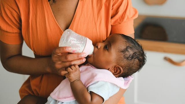 Close-up of a mother feeding her baby with a bottle in a warm home setting.