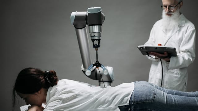 A woman receives a robotic massage as a scientist monitors, showcasing modern technology.