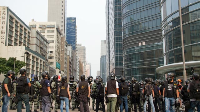 Group of police officers in anti-riot gear standing in the urban area facing a city.