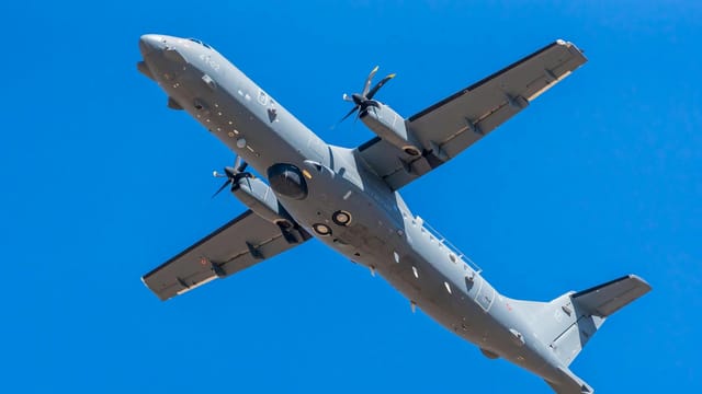 A military cargo plane flying overhead against a clear blue sky in Albacete, Spain.