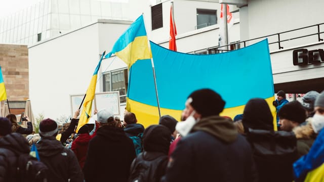 A large group of people rally outdoors holding Ukrainian flags during a peace protest.