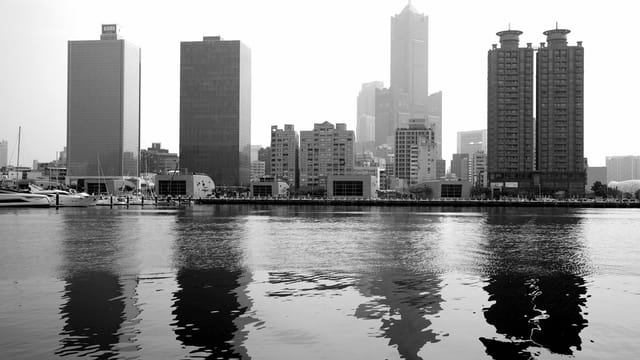 Black and white cityscape of Kaohsiung skyline with reflections on the water.