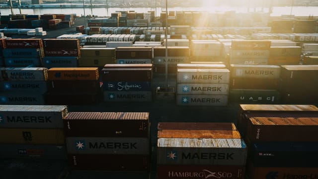From above of different colored cargo containers placed in rows in industrial district in back lit