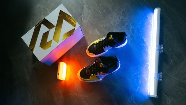 Sneakers illuminated with vibrant neon lighting on a dark marble surface for a dynamic aesthetic.