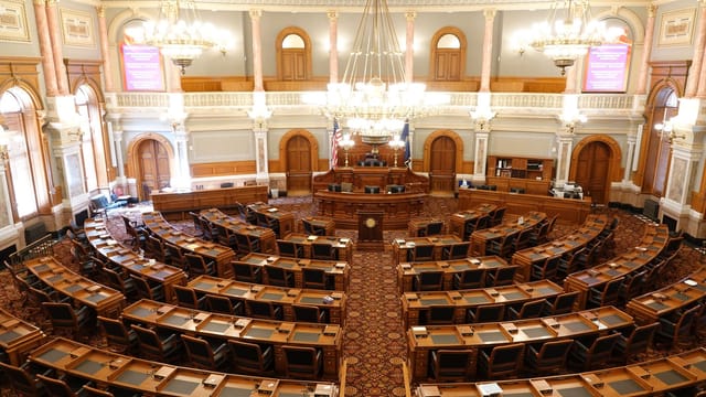 Wide view of an ornate legislative chamber with empty seats and chandeliers.