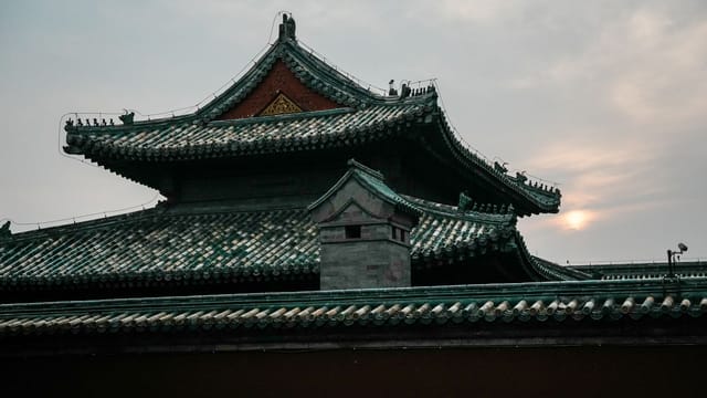 A traditional Chinese temple roof silhouetted against a serene sunset sky.