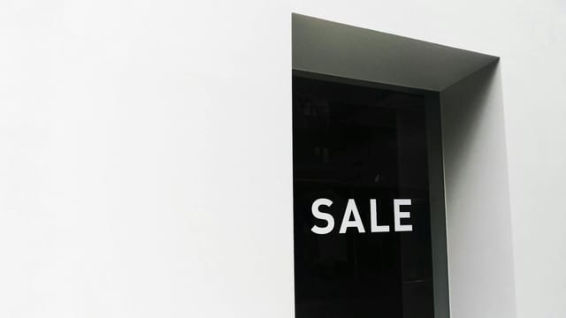 A minimalist black and white image of a sale sign on a store window with ample negative space.