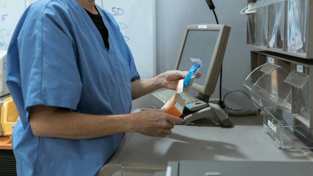 Healthcare worker in scrubs organizing medication in a medical facility.