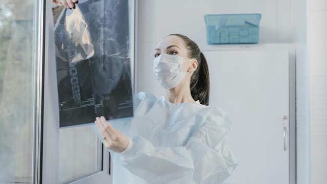 A medical professional examining an X-ray near a window in a clinical setting.