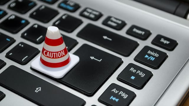 Miniature caution cone on a computer keyboard symbolizing data security and control.