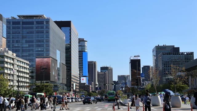 Vibrant street scene in Seoul with skyscrapers and people crossing under a clear blue sky.