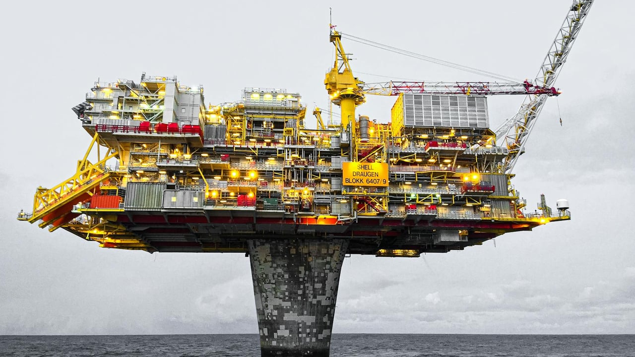 A well-lit offshore oil platform against a cloudy sky in Norway's waters.