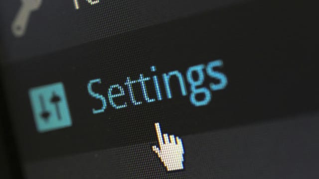 A close-up photo of a computer screen showing the settings button with a cursor hovering over it.