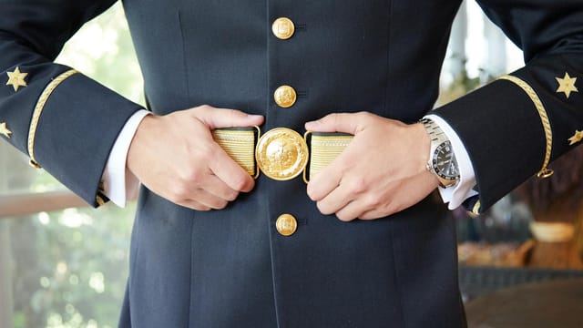 Detailed view of a person adjusting a navy uniform belt with gold embellishments.