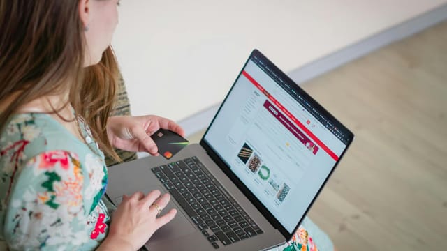 Woman in floral dress shopping online with a laptop and credit card indoors.