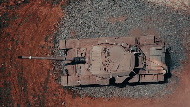 Aerial shot of a military tank parked on rugged terrain captured by drone.