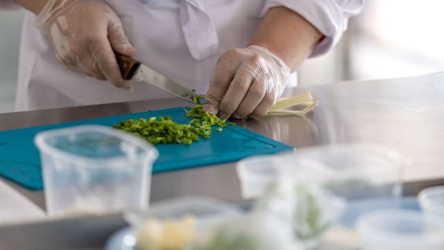 A chef expertly chops fresh herbs on a blue cutting board in a professional kitchen environment.