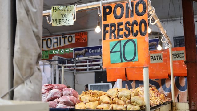Market stall displaying fresh chicken and pork with pricing sign in Spanish.