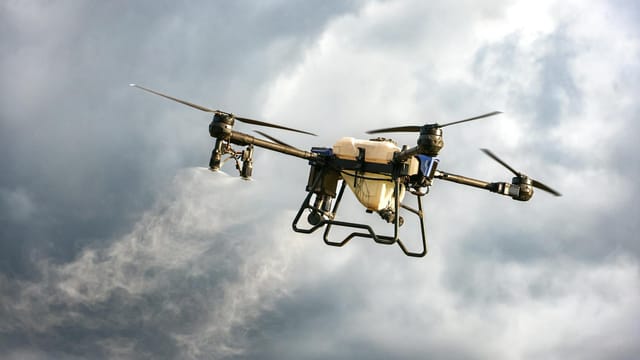 A drone dispersing mist in a cloudy sky, showcasing agricultural technology innovation.
