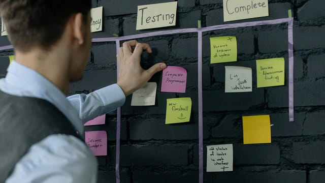 Man organizing project tasks on a wall using sticky notes in a modern office setting.
