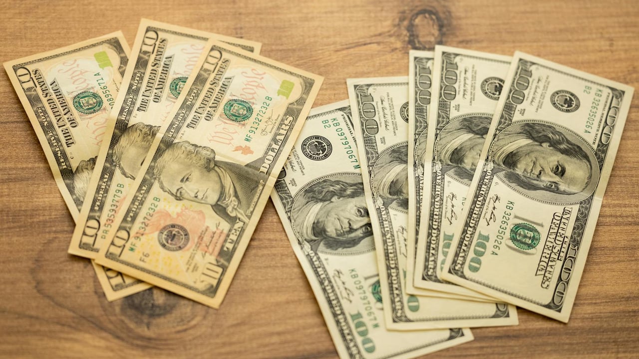 A collection of US dollar bills arranged on a wooden surface, showcasing currency denominations.